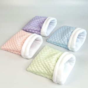 May include: Four small pet beds in pastel colors: lavender, pink, light blue, and pale green. Each bed has a quilted exterior and a white, plush interior. The beds are designed with a cozy, enclosed shape.