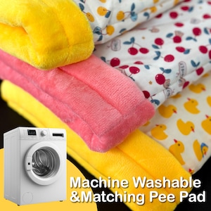 May include: A stack of soft, colorful pet pads in yellow and pink, with a white pad featuring red cherries. A yellow pad with yellow ducklings is also visible. The text "Machine Washable & Matching Pee Pad" is displayed.