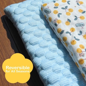 May include: Reversible bedding with a light blue textured side and a white side patterned with yellow cherries and the word "LOVEL". The text "Reversible for All Seasons" is in a yellow flower shape.