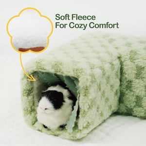 May include: A soft, light green fleece tunnel for small pets. The tunnel has a textured pattern and a cozy interior. A black and white guinea pig is inside the tunnel. Text reads: "Soft Fleece For Cozy Comfort."