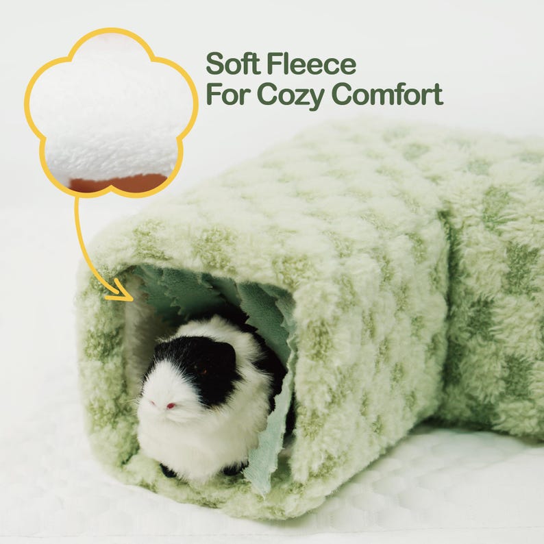 May include: A soft, light green fleece tunnel for small pets. The tunnel has a textured pattern and a cozy interior. A black and white guinea pig is inside the tunnel. Text reads: "Soft Fleece For Cozy Comfort."