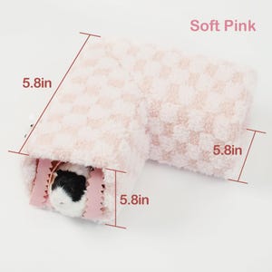 May include: A soft pink, L-shaped pet bed with a checkered pattern. The bed measures 5.8 inches on each side and features a small pet inside. The text "Soft Pink" is visible in the image.