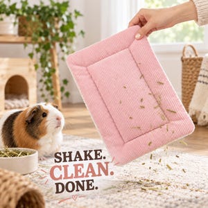May include: A rectangular pink corduroy pet mat with a white underside, being held up to shake off loose hay debris. The text SHAKE. CLEAN. DONE. is printed in brown and pink letters on the image, alongside a small guinea pig nearby.