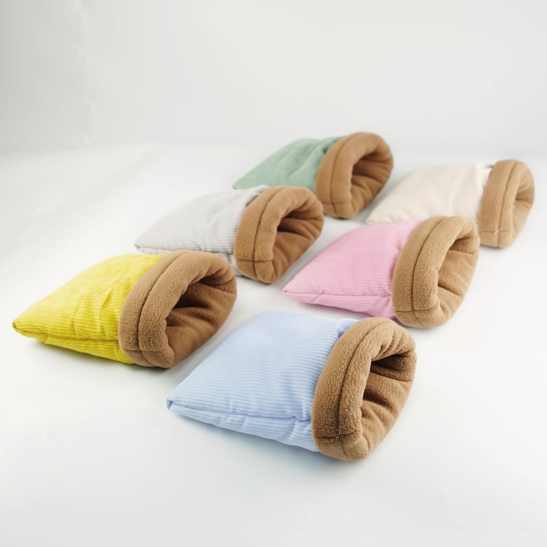 May include: A collection of small pet beds in various colors, including yellow, green, pink, and blue. Each bed has a corduroy exterior and a soft, brown, plush interior. The beds are arranged in a semi-circular pattern.