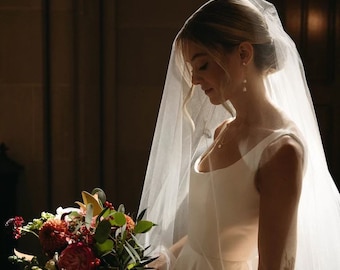 May include: A bride in a white wedding dress with a veil covering her face holds a bouquet of red, orange, and green flowers.