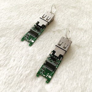 May include: A pair of earrings made from circuit boards with USB connectors. The circuit boards are green and the connectors are silver.