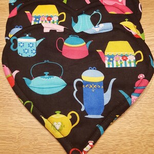 May include: Set of four black heart-shaped fabric pot holders with a colorful teapot pattern. The teapots are in various colors, including pink, blue, yellow, and green.