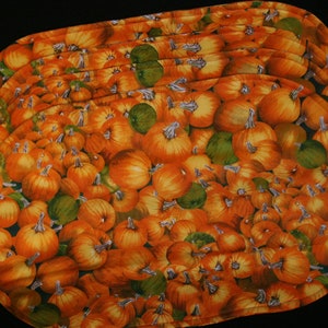 May include: A set of orange and green fabric placemats featuring a pattern of pumpkins. The placemats are made of a soft, quilted fabric and are perfect for adding a touch of fall decor to your table.