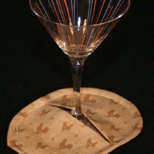 May include: A brown fabric coaster with a rooster pattern and a clear glass martini glass with orange and white stripes.