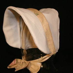 May include: A white bonnet with a floral print trim. The bonnet has a wide brim and a gathered crown.