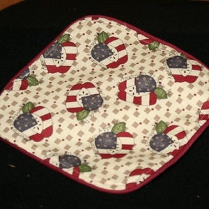 May include: A red and white patterned fabric pot holder with a cream background and a red border. The pattern features red and white apples with a blue and white star design.