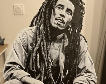 Może przedstawiać: Czarno-biała figurka Bob Marley'a z dredami, ubrana w koszulę i spodnie, wydrukowana w 3D. Figurka stoi na małym drewnianym stojaku.