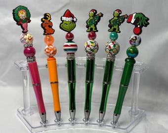 Può includere: Sei penne con topper a tema natalizio, inclusi personaggi e icone festive. Ogni penna ha un colore del fusto unico, come rosa, arancione e verde, accentuato da perline decorative con vari motivi, colori e distanziatori color argento.