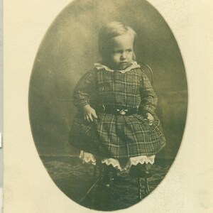 小さな椅子に座っているチェック柄のドレスを着た不機嫌な女の赤ちゃんのポートレート RPPC 実写ポストカード写真 白黒写真