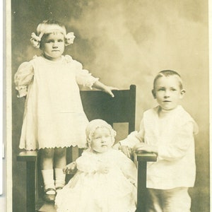 Alarm Baby Mädchen sitzend mit Bruder Schwester stehend 1910er Jahre Antik RPPC Echtes Foto Postkarte Fotografie Schwarz Weiß Foto