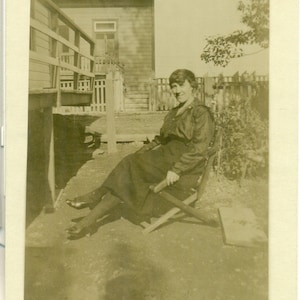 1920s Flapper Trying to Pose Outside in Folding Chair Holding Onto Side RPPC Postcard Vintage Photo Photograph