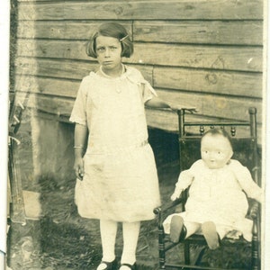 Fille debout gros bébé poupée assis sur une chaise à l'extérieur Antique RPPC Photo réelle carte postale vintage photographie