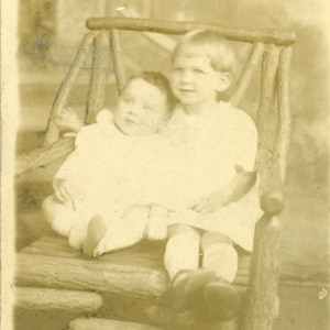 Fière grande sœur tenant bébé sur une chaise en rondins Frères et sœurs ensemble RPPC Real Photo Postcard AZO