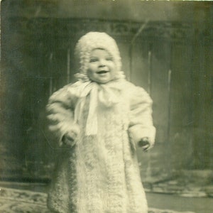 1909 年のクリスマス、ニットの毛皮のコートとボンネットを着て立っている女の赤ちゃん、アンティーク RPPC 実写ポストカード
