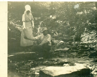 1910s Man Sitting by Stream Handing Bottle to Bonnet Woman RPPC Real Photo Photo Black White Photo