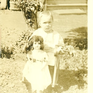 Baby Holding Doll Bunch di Fiori Seduto a Rocking Sedia Piccolo Ragazzo 1910s RPPC Reale Foto Cartolina Foto Foto Nero Bianco Foto