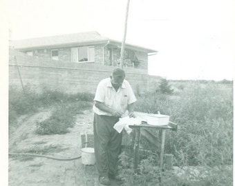 Man Cleaning Fish at Table by House Fishing Cutting Gutting Filet With Hose Pans 1950s Vintage Black and White Photo Photograph