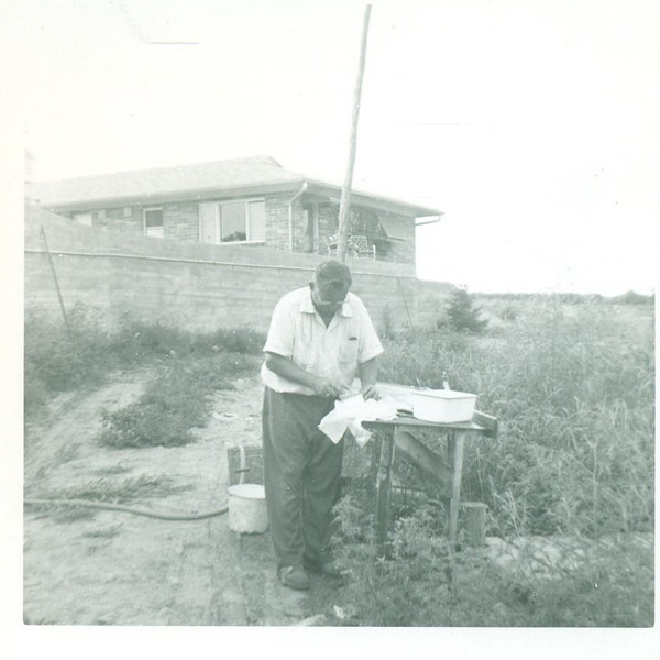 Man Cleaning Fish at Table by House Fishing Cutting Gutting Filet With Hose Pans 1950s Vintage Black and White Photo Photograph