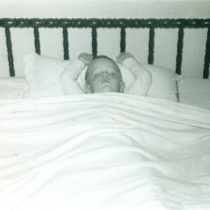 1950s Boy Sleeping With Arms Above Head on Pillow Big Bed Photo Black White Photograph
