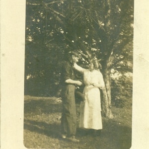 Madre llegando a arreglar el cabello de un hijo alto para una imagen debajo del árbol 1910s RPPC Fotografía de postal fotográfica real