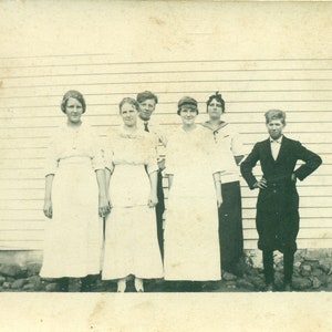 1900er Jahre 4 Schwestern weiß Kleid kleine Bruder Hände auf Hüften schwarz Knickers Anzug RPPC echte Foto Postkarte Foto schwarz weiß Foto Antik