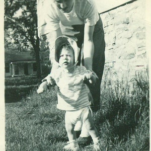 Niet zo gelukkig wandelen baby meisje luier bonnet opgehouden door moeder jaren 1940 vintage zwart wit fotofoto
