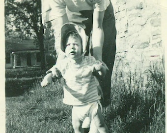 Not So Happy Walking Baby Girl Diaper Bonnet Held Up By Mother 1940s Vintage Black White Photo Photograph