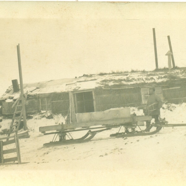 Nome Alaska Winter 1909 Freight Sled Sod Roof Building Man Holding Snowshoes RPPC Real Photo Postcard Antique Black White Photo