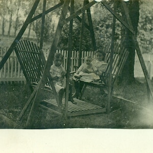 Menina segurando brinquedo de boneca em balanço de madeira com irmãozinho 1910s RPPC Foto real Cartão postal Foto preta e branca