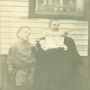 Irmão mais velho entediado em pé com o bebê do lado de fora da janela da casa da fazenda 1900 RPPC Foto real de cartão postal