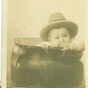 Hijo del médico, bebé sentado en una bolsa de médico negra con sombrero en la mesa AZO Antique RPPC Foto real Postal