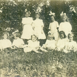 Unladylike Little Girls Sitting in Grass White Dress Hair Bows Playing Antique RPPC Real Photo Postcard Photograph Black White