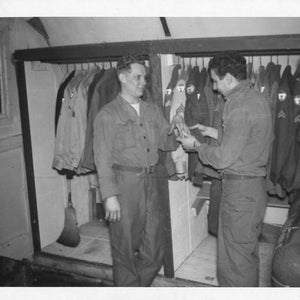 Peut inclure: Deux personnes se tiennent dans une pièce avec un rack de vêtements. La personne à gauche porte une chemise foncée et un pantalon. La personne à droite porte une chemise claire et un pantalon foncé. Le rack est rempli de vestes et de manteaux.