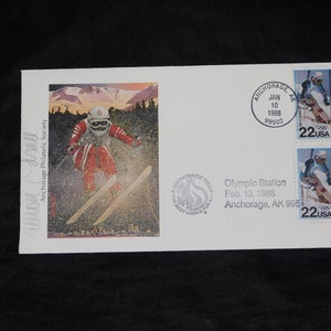 May include: White envelope with a colorful illustration of a skier in red and white ski gear. Two 22-cent USA stamps feature a skier. The envelope is postmarked "Anchorage, AK" with the date "Jan 10, 1988".