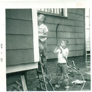 1957 Bruder nehmen Ziel mit Garten Schlauch Junge auf Leiter Jungen spielen außerhalb Foto schwarz weiß Foto