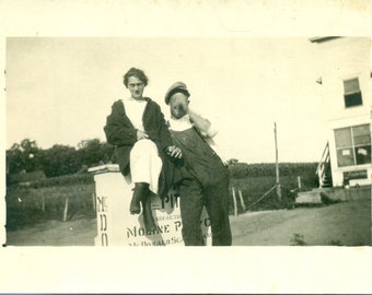 Farmer Making A Funny Face With Hand And Wife Sitting on Factory Sign Summer 1920s RPPC Postcard Vintage Photo Photograph