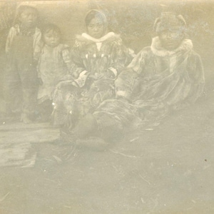 Antico Akutan Alaska nativo Aleut uomo donna foto seduta fuori tradizionale pelliccia parka abbigliamento bambini in piedi sul portico a guardare fotografia