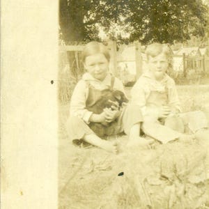 Bauernhof Jungen Halten einen Welpen draußen Sitzen Barfuß Overalls Kinder Brüder Antike RPPC Echtfoto-Postkarte