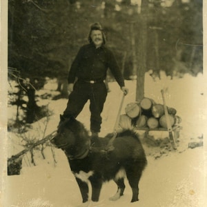 Fotografia antica di un uomo dell'Alaska che trasporta legna su una slitta trainata da cani, cappello da cacciatore di pellicce sulla neve invernale