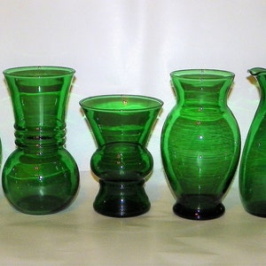 May include: A collection of nine green glass vases of various shapes and sizes. The vases are all made of a dark green glass and have a smooth, polished finish.