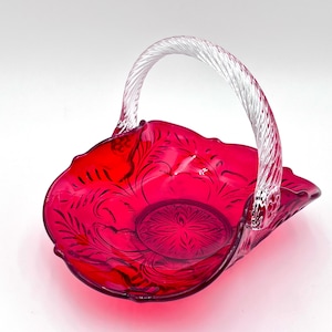 May include: A red glass basket with a clear twisted handle. The basket has a decorative etched design.