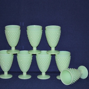 May include: Eight green milk glass goblets with a textured, raised dot pattern. The goblets are stacked in a pyramid shape with one goblet lying on its side.