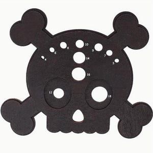 May include: Black skull-shaped tool with numbered holes of different sizes. The tool is made of wood and has a textured surface.