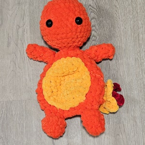 May include: A crocheted orange and yellow plush toy with black eyes. The toy is shaped like a small creature with a round body and a tail.