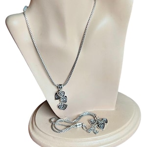 Może przedstawiać: Srebrny naszyjnik z łańcuszkiem i zawieszką w kształcie pięciu splecionych serc. Serca są czarne z srebrnymi obw&oacute;dkami. Naszyjnik znajduje się na manekinie.